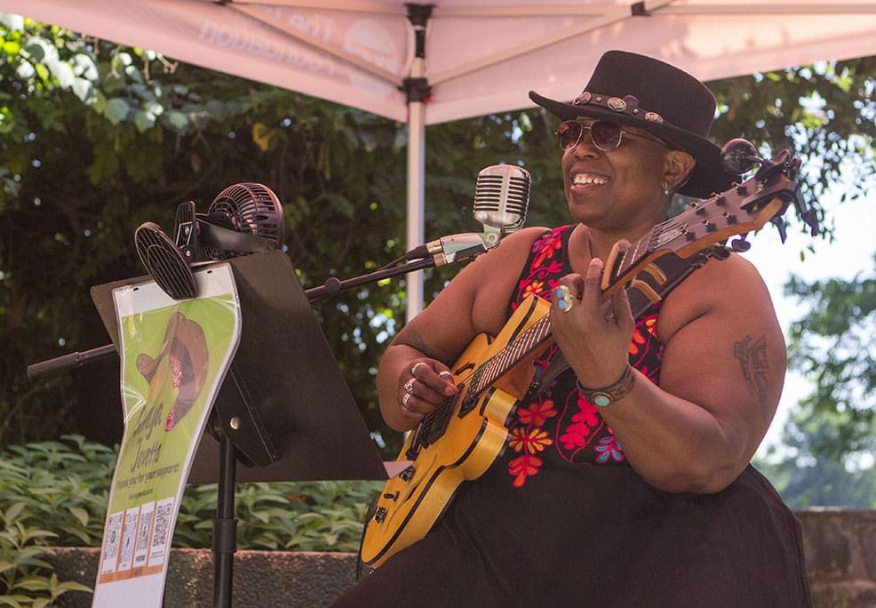 A woman smiles while playing the guitar under an orange tent